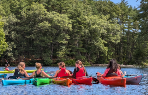 children kayaking on a pond surrounded by forest