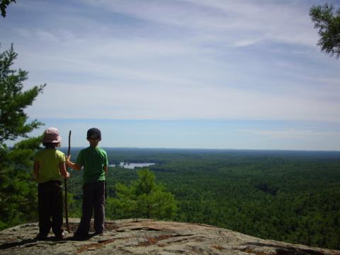 Two children stand looking out at a view after a hike. 